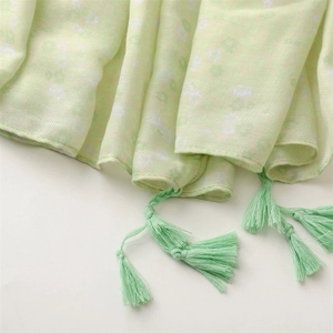Detail of light green linen scarf with white floral patterns and woven fringe tassels