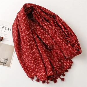 Détail d'une écharpe en lin rouge avec motifs floraux blancs et pompons sur fond blanc