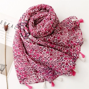 Detail of floral printed scarf with pink and white tassels on a light linen fabric