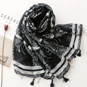 Detail of black and white paisley print scarf with fringe tassels on white background