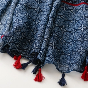 Detailed macro of ethnic floral shawl with blue geometric patterns and vibrant red tassels