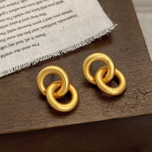 Détail de boucles d'oreilles créoles géométriques mates en or sur une surface en bois