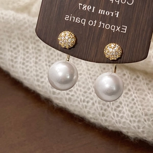 Detail of vintage gold pearl earrings with micro-set zircon spheres on wood background