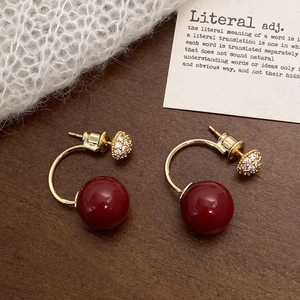Vintage C-shaped gold earrings with red pearls and zircon accents on a textured background