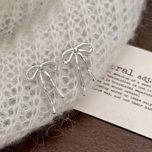 Detail of silver bow earrings resting on white knit fabric with an aesthetic card