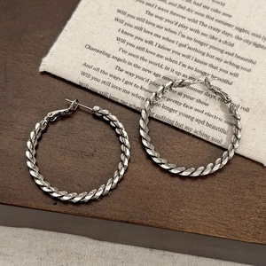 Orecchini a cerchio intrecciati argento con texture su sfondo vintage rustico