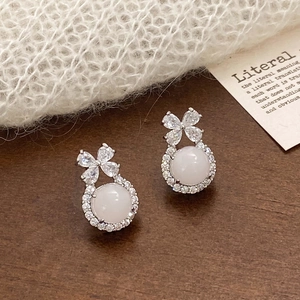 Detailed close-up of bow-knot chalcedony earrings with zircon inlay on a wooden desk