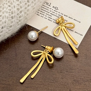 Elegant gold bow pendant pearl stud earrings displayed on a soft textured background