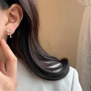 Elegant gold bow earrings with cubic zirconia and small pendant on female model