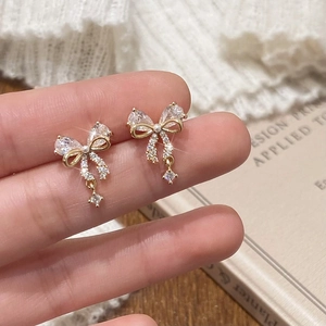Elegant gold bow earrings with micro pearls and zircon displayed on a soft knit background