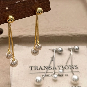 Macro shot of gold and silver tassel earrings with champagne pearls on wood display
