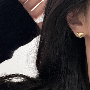 Close-up of heart-shaped gold stud earrings featuring a unique hammered metal texture on ear