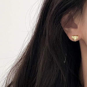 Close-up of heart-shaped gold stud earring with hammered texture on model's ear