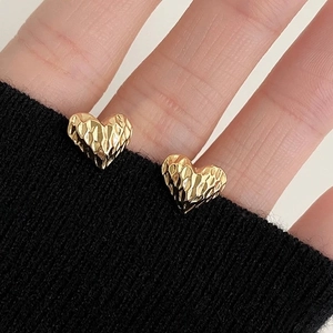 Detailed close-up of gold heart stud earrings with a textured hammered metal surface finish