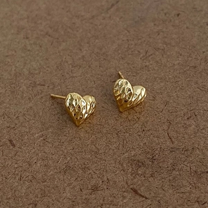 Detail view of heart-shaped gold stud earrings featuring a textured diamond-cut surface