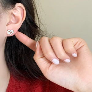 Detail of a minimalist gold and white heart knot stud earring worn by a female model