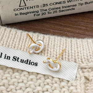 French vintage style gold knot stud earrings with white enamel on a cozy background
