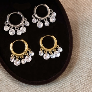 Close-up of gold and silver hoop earrings with five hanging cubic zirconia on a brown tray