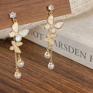 Macro shot of gold butterfly tassel earrings with white pearls and sparkling small diamonds