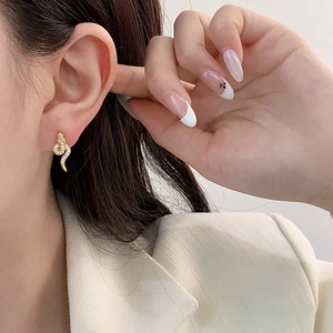 Detailed view of elegant gold snake earrings with white crystals on a model's ear