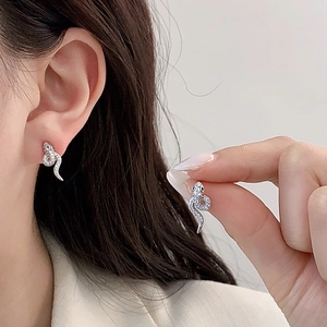 Detailed close-up of crystal-encrusted silver snake stud earrings on model's ear
