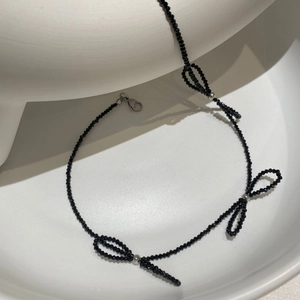 Elegant black crystal beaded bow necklace with stainless steel accents on white pedestal
