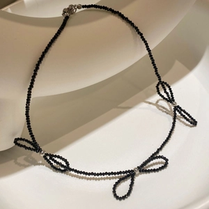 Elegant black faceted crystal beaded necklace with three bow designs on a white pedestal