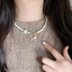 Elegante Perlenkette mit weißem Blumenanhänger und Goldakzenten auf warmem Pullover