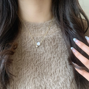 Elegant gold pearl necklace with zircon pendant worn on a warm brown sweater