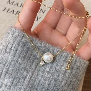 Golden pearl and zircon necklace displayed on a grey sweater sleeve background