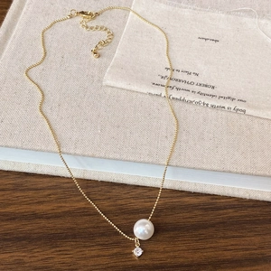 Detail view of a gold pearl necklace with zircon pendant on a natural linen fabric