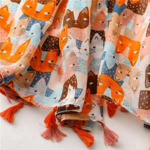 Dettaglio di sciarpa in cotone e lino con stampe di gatti e nappe colorate