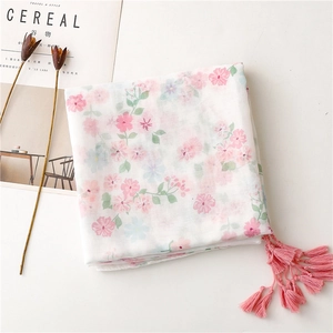 Detail of white scarf with pink floral pattern and tassel trim against minimal backdrop