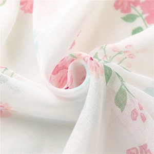 Close-up of white linen-feel scarf featuring soft pink floral patterns and delicate fringe