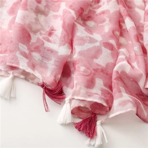 Gros plan du motif floral rose sur écharpe en gaze respirante avec pompons rouges et blancs