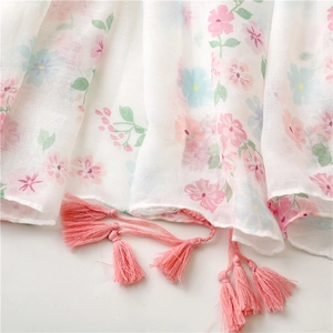 Detail of white cotton scarf featuring pink floral patterns and delicate fringe edge