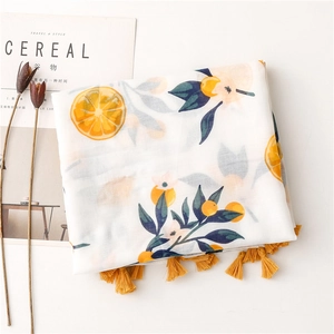 Detail view of orange fruit print scarf with yellow tassels on cotton linen fabric