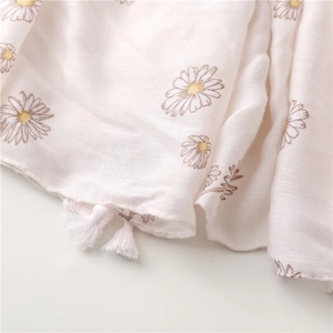 Dettaglio dello scialle bianco con stampe di margherite gialle e nappe di cotone sui bordi