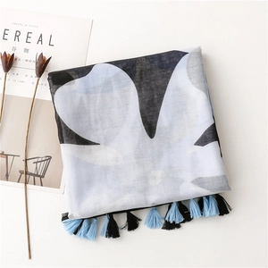 Detail of white cotton scarf with black leaf print and blue tassel trim on a table