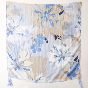 Dettaglio macro della stampa floreale blu e beige su sciarpa di lino con nappe fini