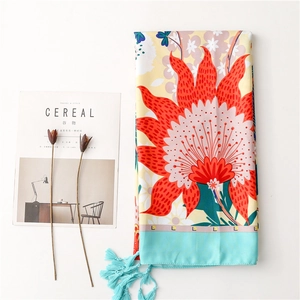 Detailed flat lay of a yellow silk shawl with red floral prints and blue fringe tassels