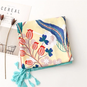Close-up of yellow floral silk scarf with blue tassels and botanical patterns