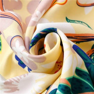 Close-up of a floral silk scarf with yellow base and twill texture in a rose fold