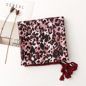 Close-up of leopard print silk scarf with burgundy tassels on a minimalist background