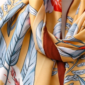 Macro shot of yellow twill silk scarf with blue feathers and red floral patterns