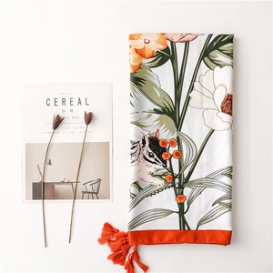 Detailed view of floral squirrel print scarf with vibrant orange fringe tassels