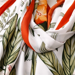 Macro detail of twill silk scarf showing floral patterns and orange hand-stitched edges