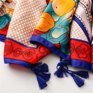 Detail of silk scarf showing orange floral prints, geometric patterns and blue tassels