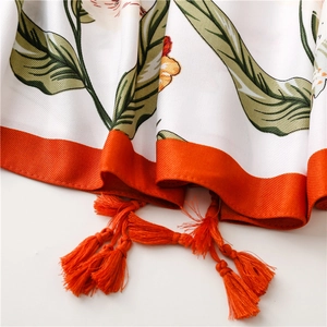 Detailed macro view of white floral scarf featuring orange tassels and twill fabric texture