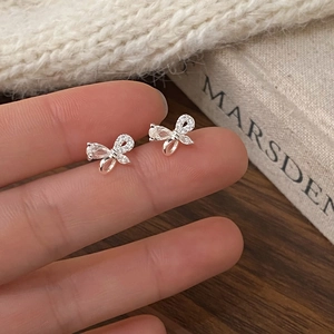 Détail d'une boucle d'oreille nœud en argent sertie de zircons tenue sur un doigt